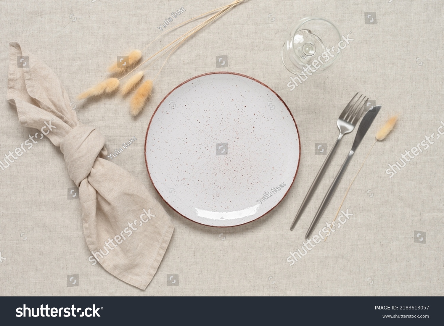 Autumn table setting. A white plate, cutlery and dry grass lagurus on a beige linen textile background. Top view, flat lay. Selective focus. #2183613057