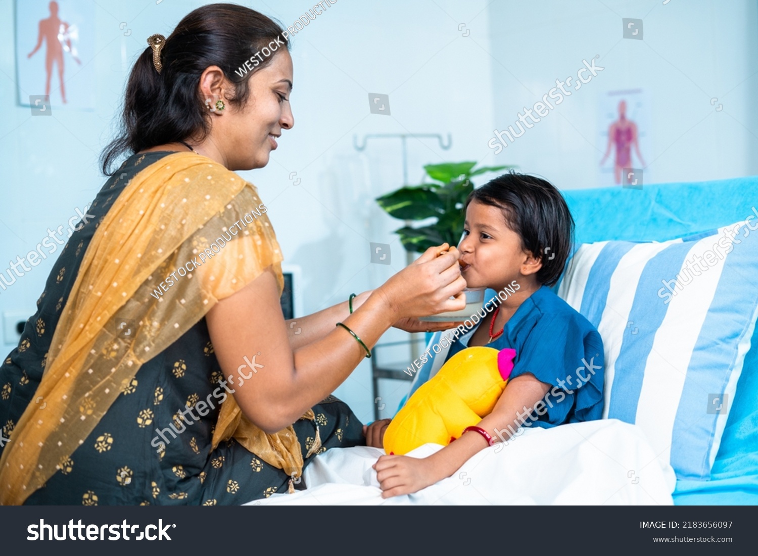 Mother feeding porridge to ill kid while admitted at hospital ward - concept of parental caring, medical treatment and health care. #2183656097