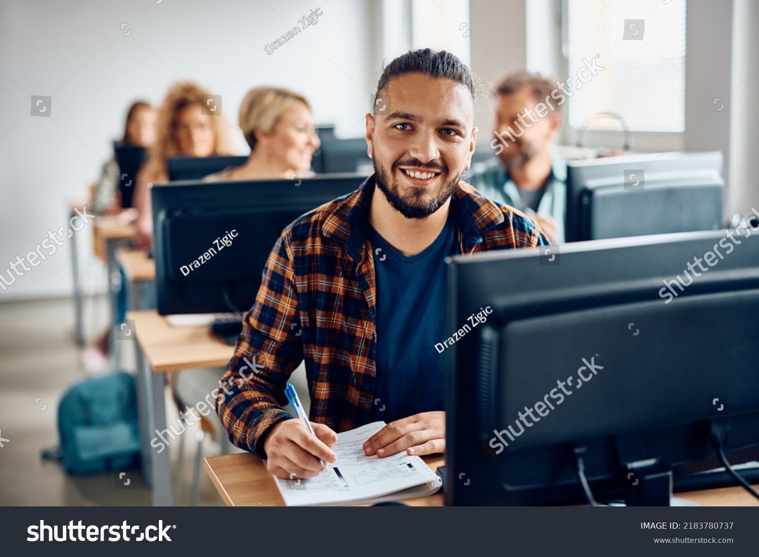 Happy college student attending computer class and taking notes while looking at camera. #2183780737