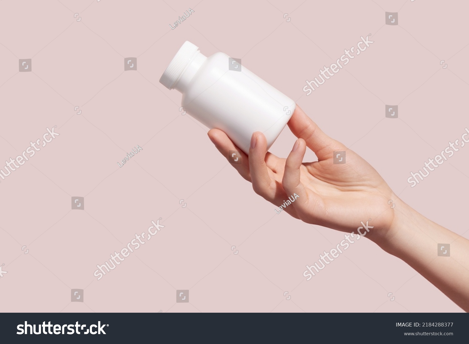 Female hand holding blank white squeeze bottle plastic tube on pink background. Packaging for pills, capsules or supplements. Mockup. High quality photo #2184288377