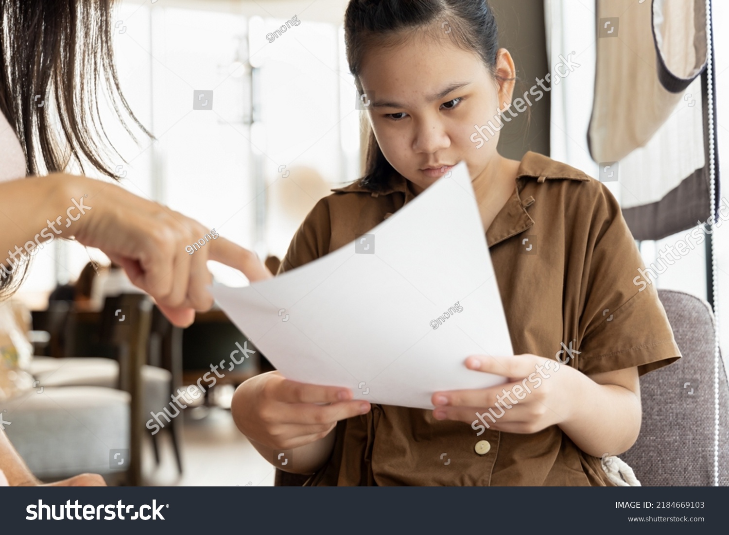 Asian mother hand pointing at poor grading from examination result report of her daughter #2184669103