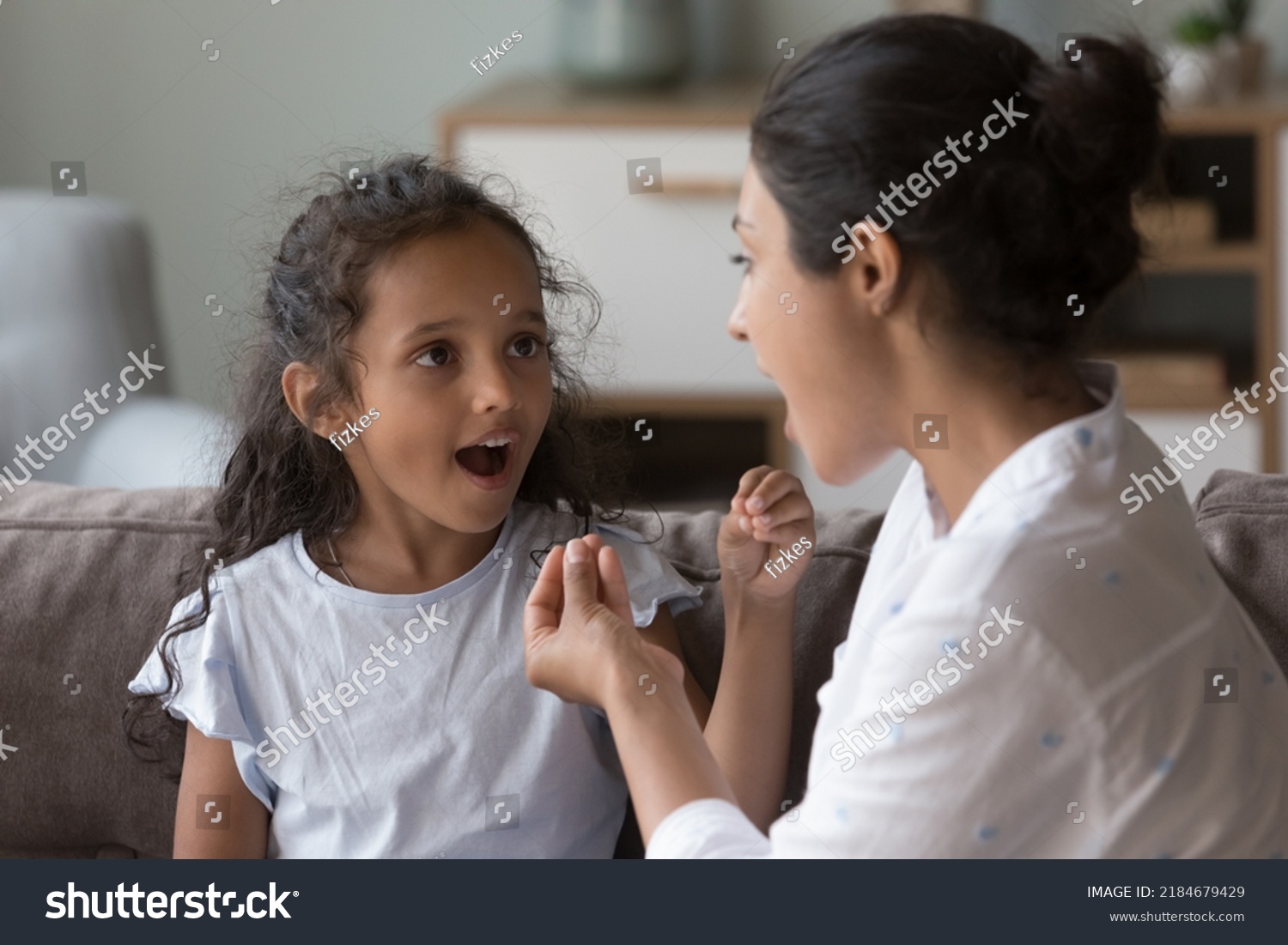 Indian female therapist training kid with hearing disability, deafness to use fingers for communication. Mom and cute daughter kid speaking sign language, talking, using hand gestures #2184679429