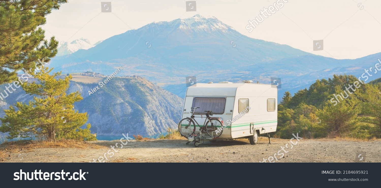 Caravan trailer parked on a mountaintop with a view on French Alps near lake Lac de Serre-Poncon. Transportation, RV, motorhome, road trip, camping, tourism, recreation, lifestyle #2184695921