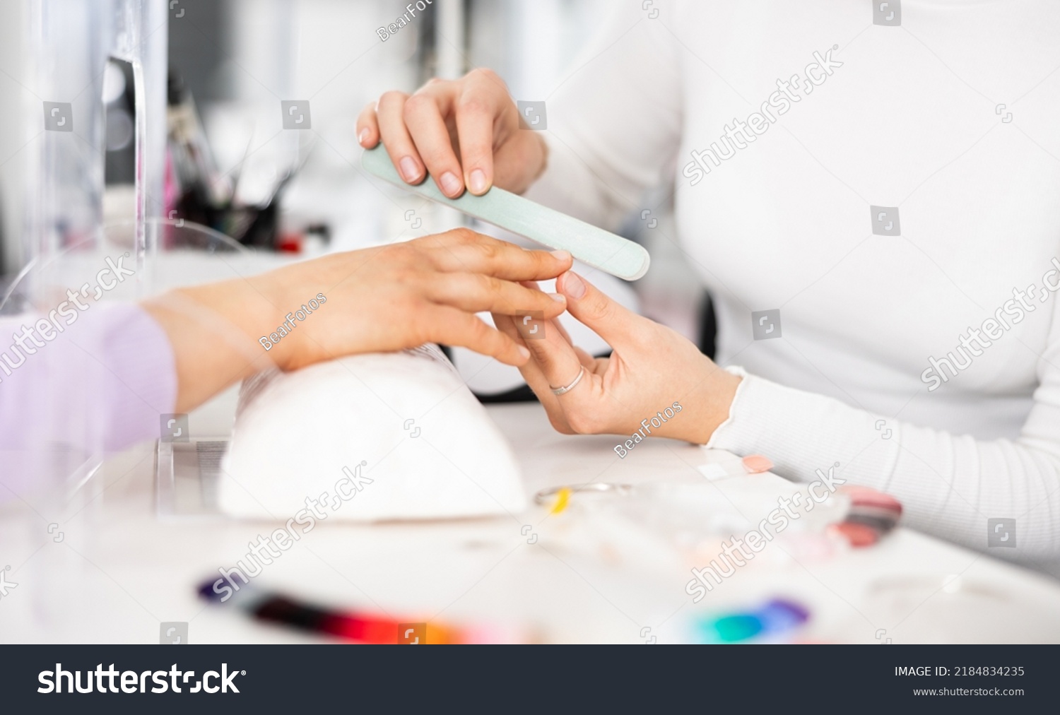 Young woman hands in a nail salon, which the manicure master files the nails with a nail file, giving them shape #2184834235