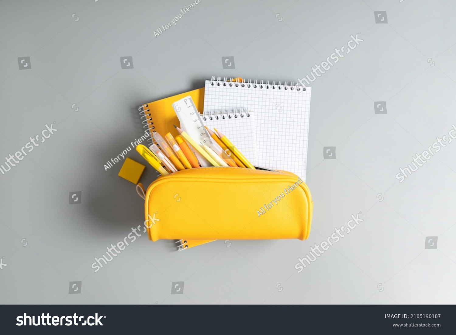 Back to school concept. Yellow school pencil case with filling school stationery, notebook, pens, pencils. Yellow school accessories on grey background. Flat lay, top view, copy space #2185190187
