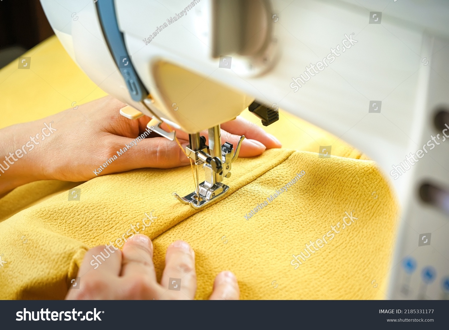 Seamstress female hands holding and stitching yellow textile fabric on modern sewing machine at workplace. Sewing process, upholstery, clothes, repair, DIY. Handmade, hobby, small business concept #2185331177