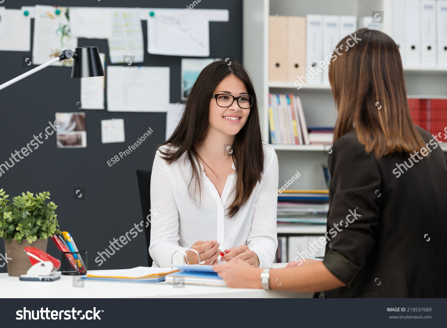 Two young businesswomen having a meeting in the office sitting at a desk having a discussion with focus to a young woman wearing glasses #218537689