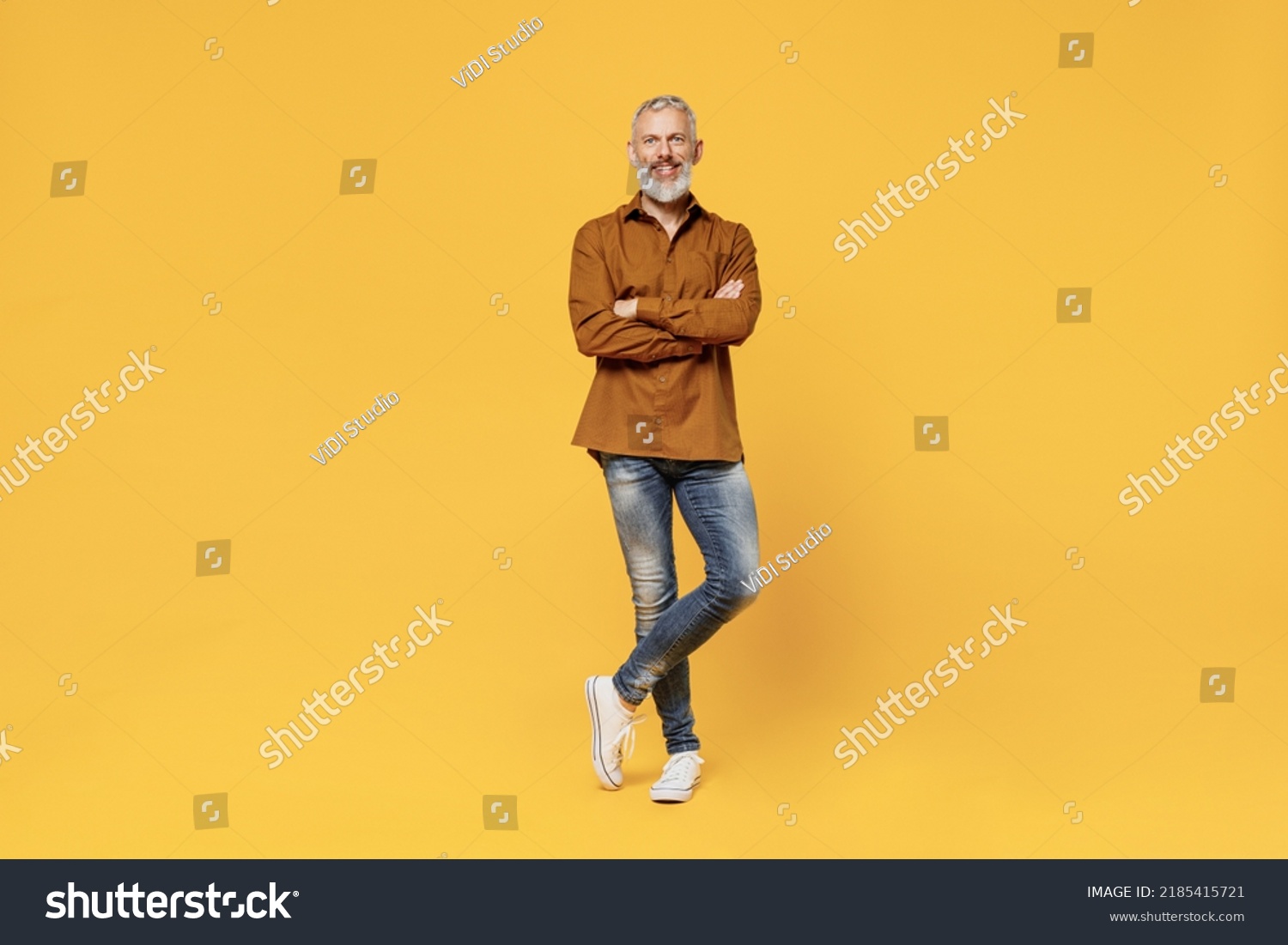 Full size body length excited charismatic elderly gray-haired bearded man 40s years old wears brown shirt looking camera smiling keep hands crossed isolated on plain yellow background studio portrait #2185415721