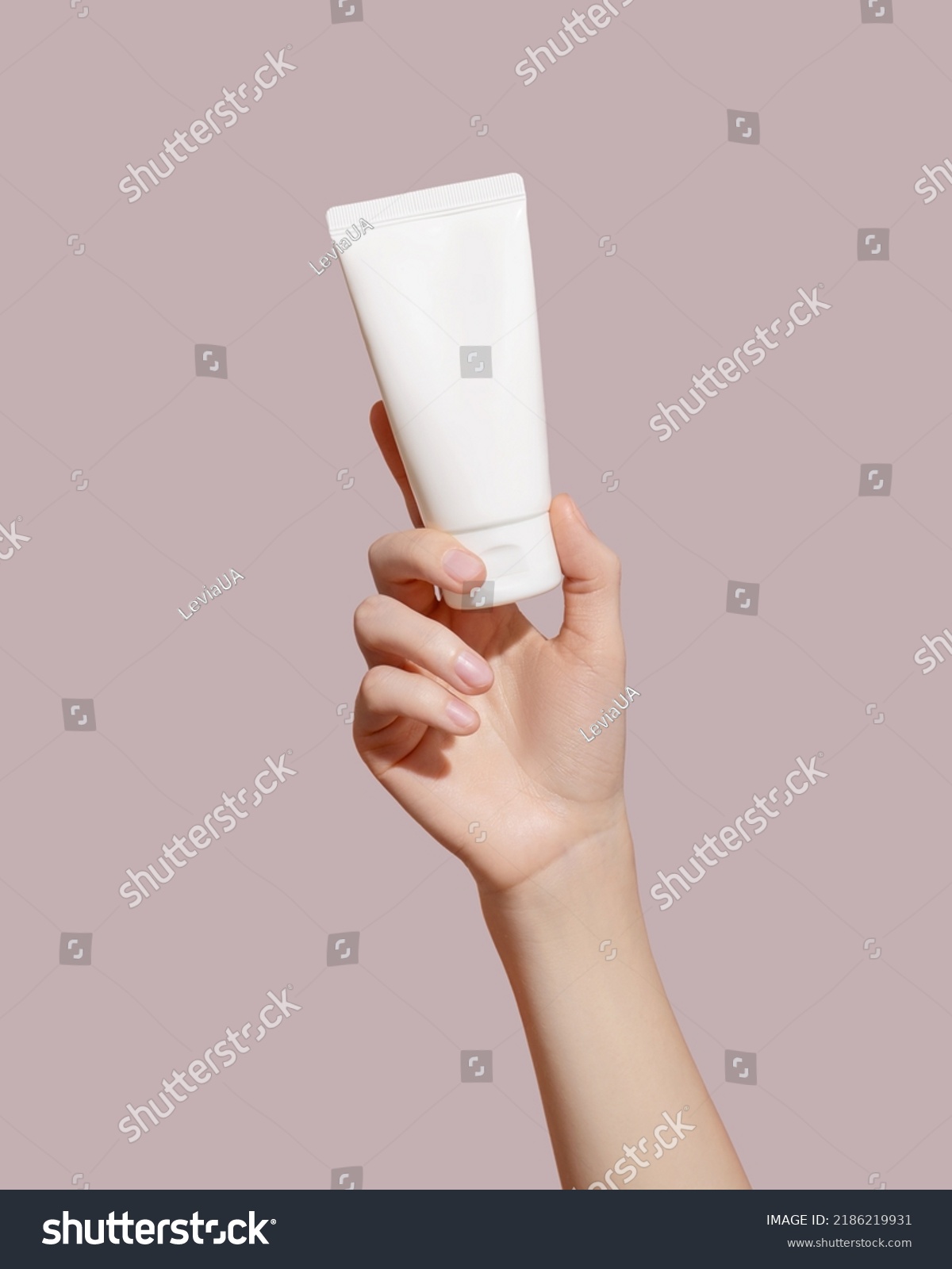Hand holding blank white plastic tube on pink background. Cosmetic beauty product branding mockup. Copy space. High quality photo #2186219931