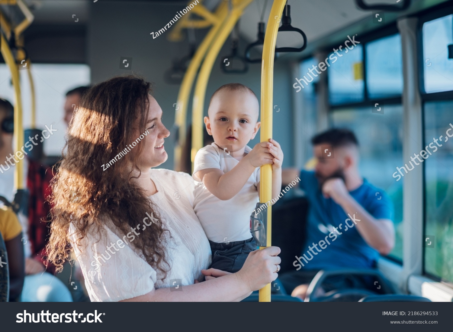 Mother carries her child while standing and holding on to the bus.Mom holding her infant baby boy in her arms while riding in a public transportation. Cute toddler boy traveling with his mother. #2186294533