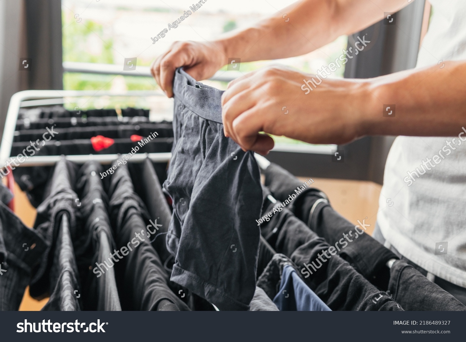 Close up image of a person's hands hanging underwear on a metal indoor clothesline. Householder doing housework happy and content to feel fulfilled. Man completing the laundry. #2186489327
