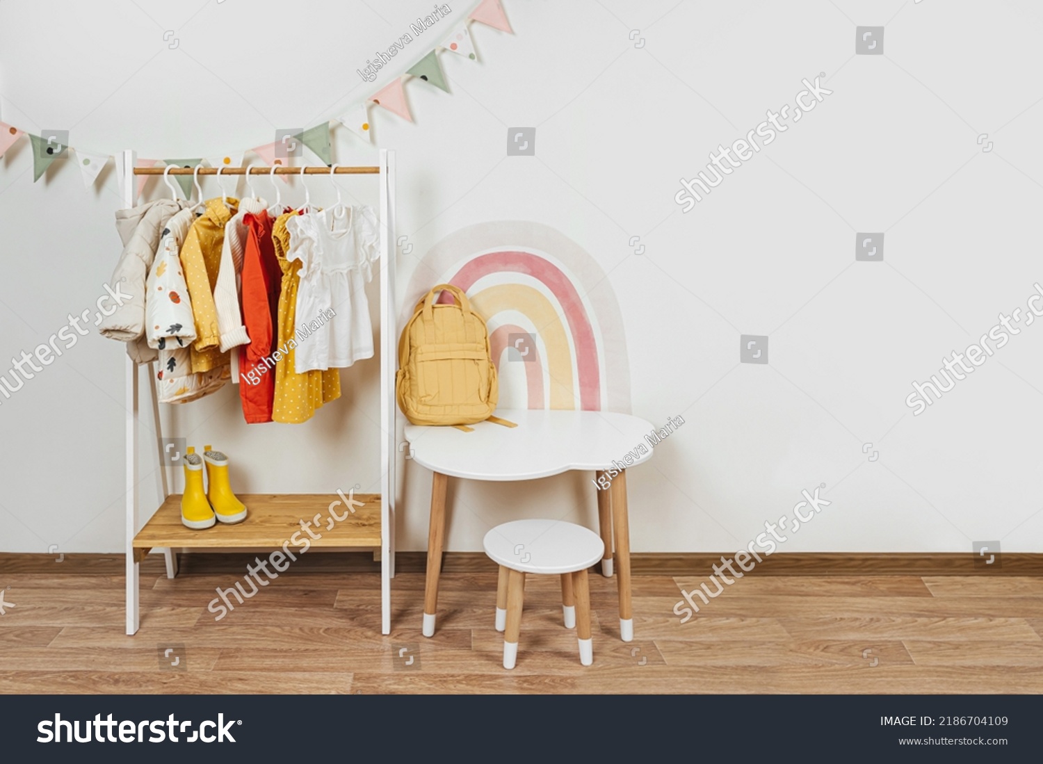 Children's room with Montessori Clothing Rack, white table and rainbow. Dress, jacket and sweaters on hangers in wardrobe. Nursery Storage Ideas. Montessori Toddler Room #2186704109