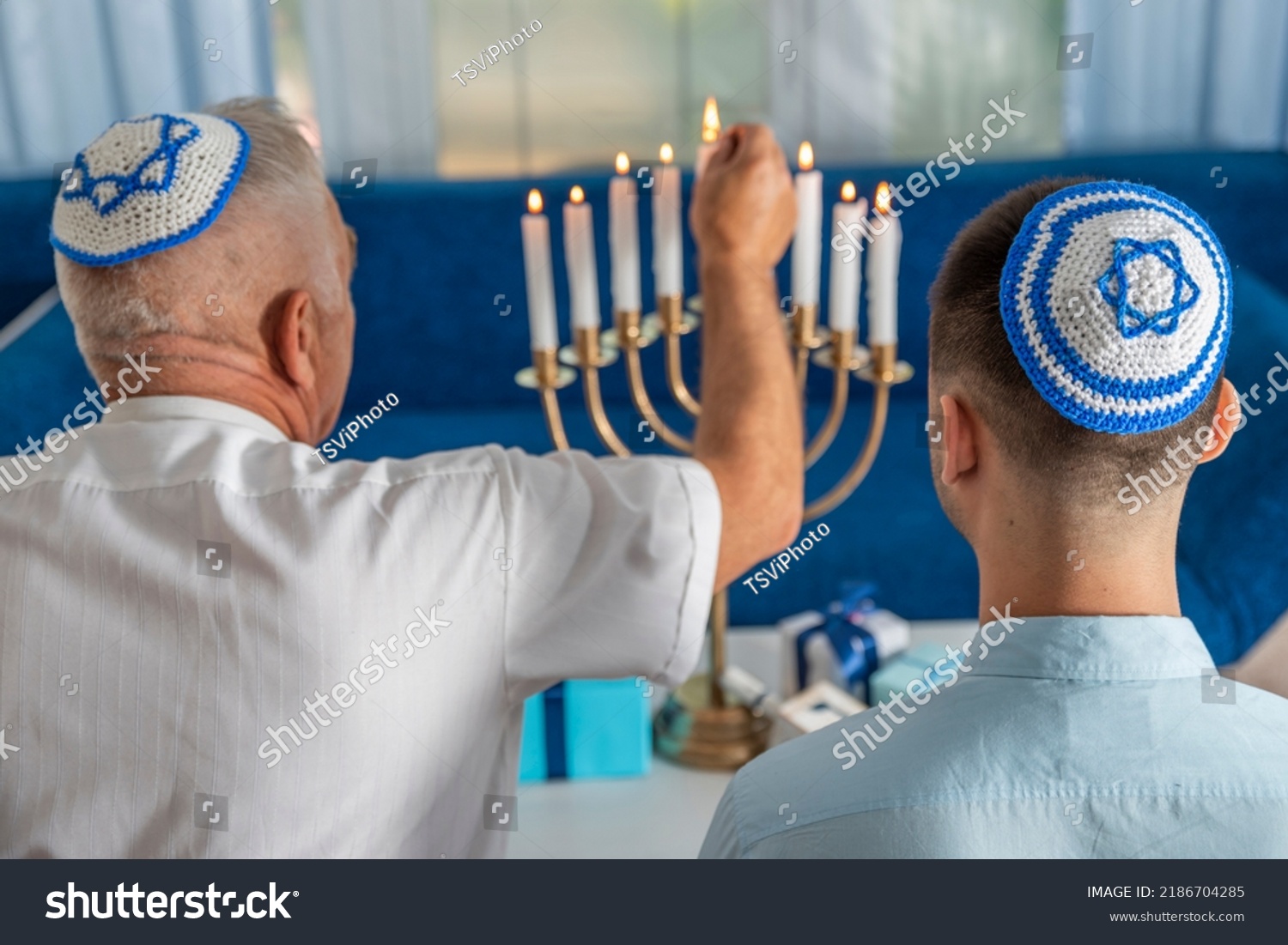 Hanukkah holiday. A senior man and young guy wear kippahs on heads in front of Jewish Hanukkah Menorah, lighting fire of candles. Yarmulke with Star of David. Traditional Hebrew Festival of Lights. #2186704285