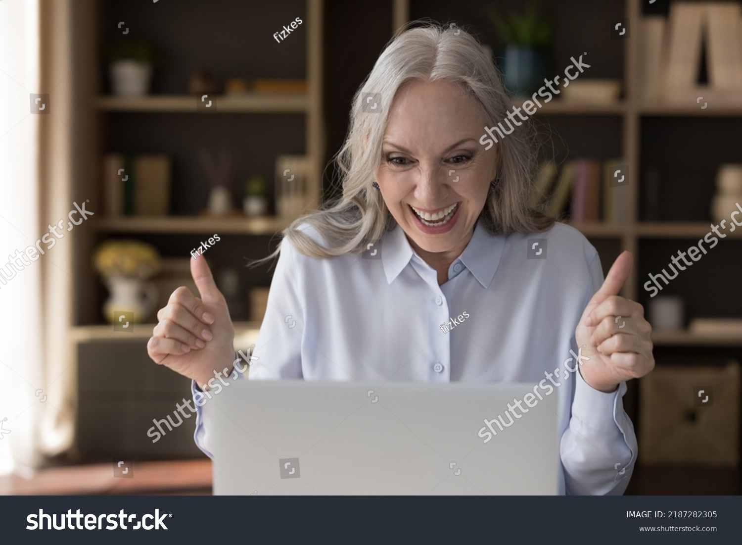 Happy amazed senior laptop user woman getting exciting good news from online chat, email letter, notice, video call, looking at screen, staring at monitor, laughing, smiling, making winner hands #2187282305