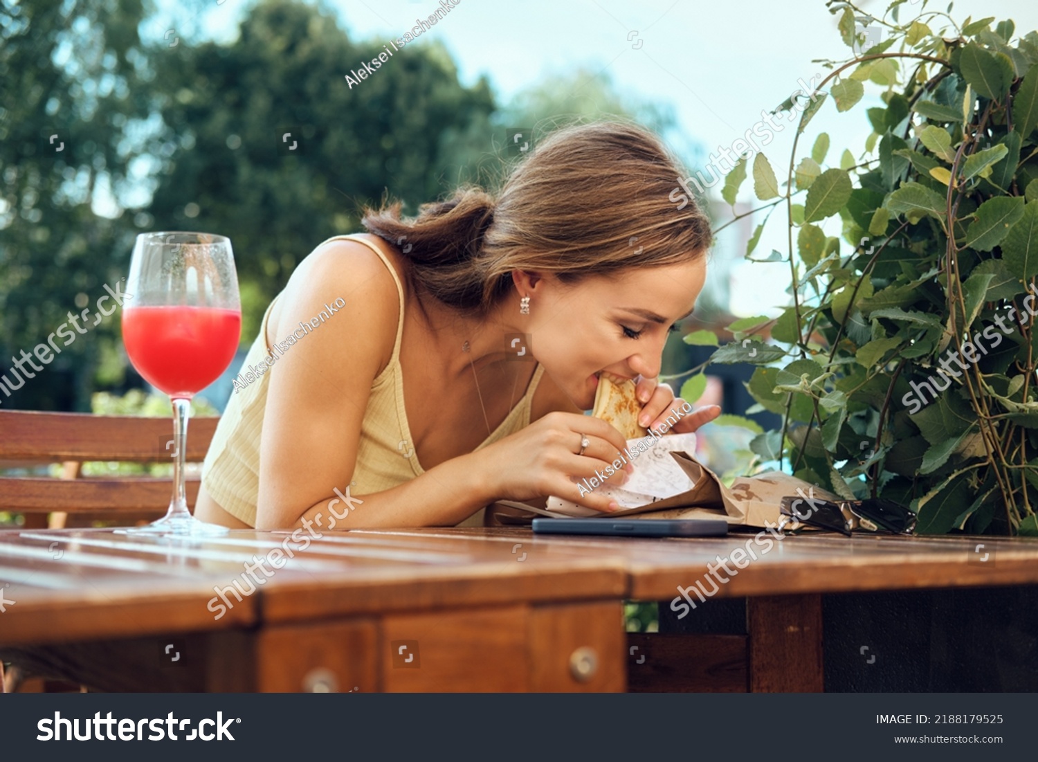 Young woman bites slapjack stuffed with bacon, ham and cheese sitting at outdoor terrace #2188179525