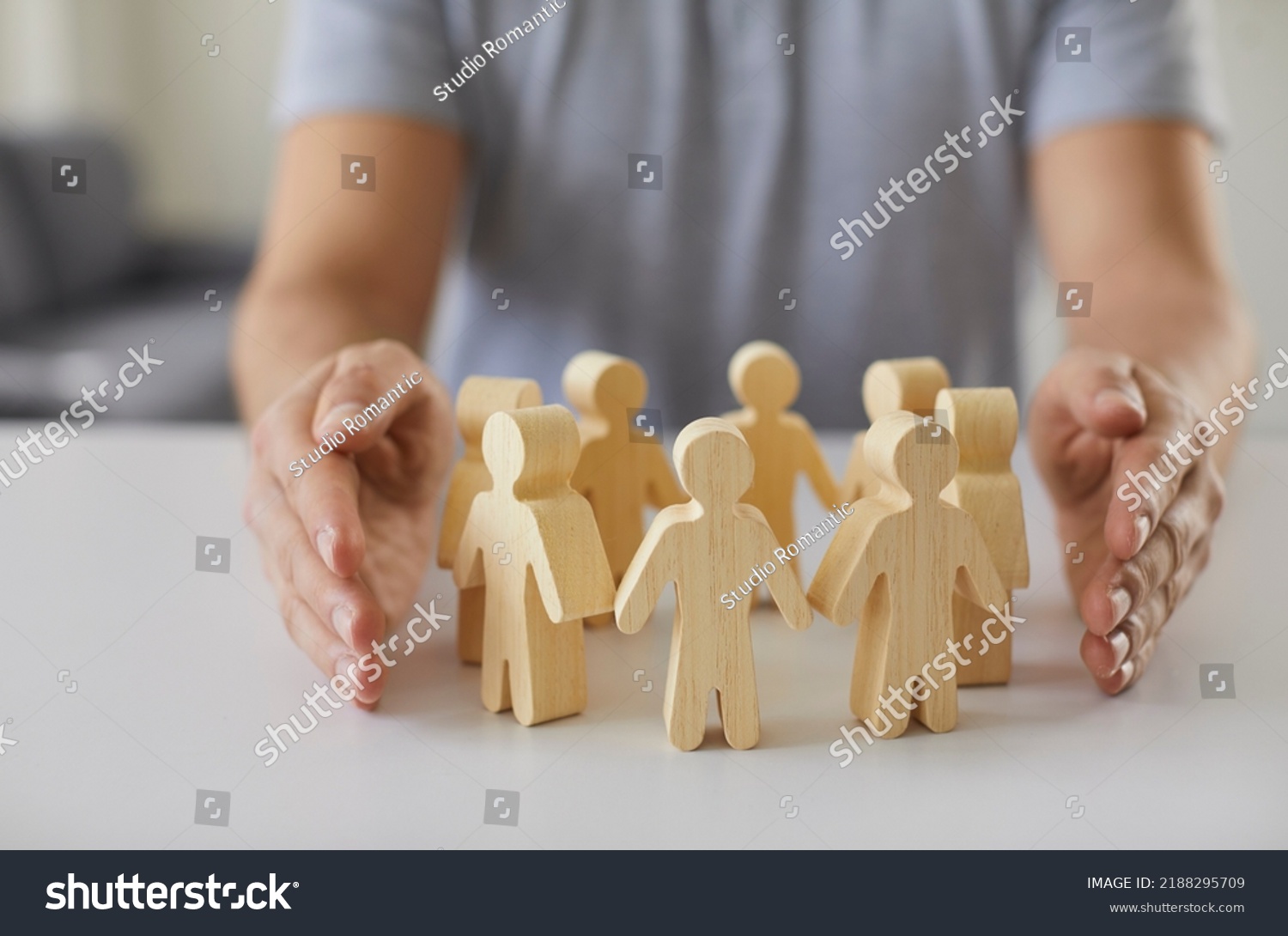 Social protection. Wooden figurines of people surrounded by man's hands symbolizing care for employees, customers or family. Close-up of figurines of people standing in circle on table and male #2188295709