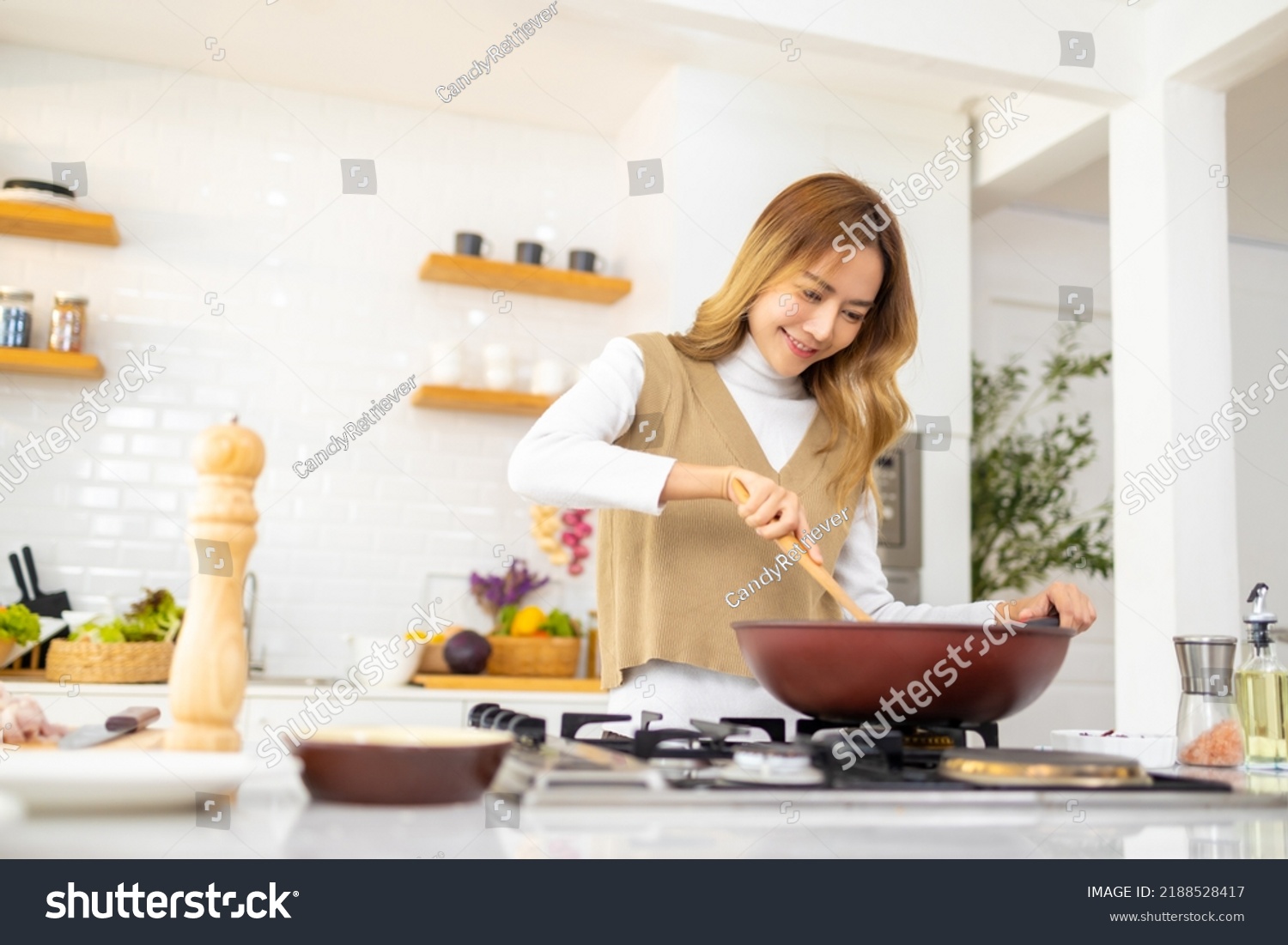 Young beautiful Asian woman enjoy cooking healthy food and pasta in cooking pan on stove in the kitchen at home. Happy female having dinner meeting party celebration with friends on holiday vacation. #2188528417
