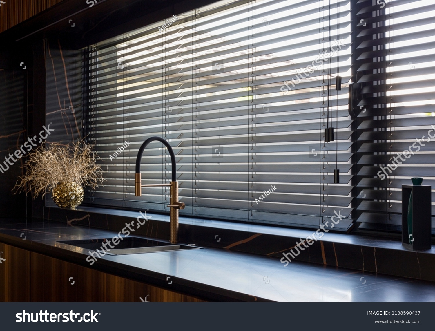 Wooden blinds black color closeup on the window. Bamboo slats 50mm wide. Venetian wood blinds in the kitchen. Black tapes. Sink with copper faucet near the window. Round vase is on the windowsill. #2188590437