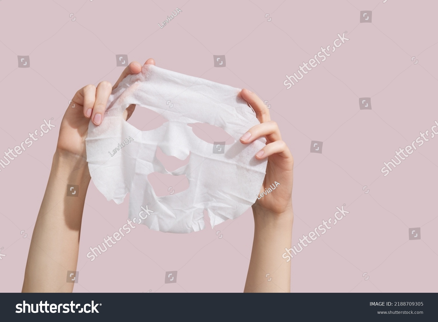 Female hands holding sheet of white mask on pink background. High quality photo #2188709305