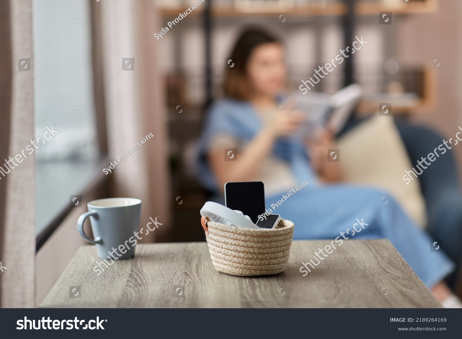 digital detox and leisure concept - close up of gadgets in basket on table and woman reading book at home #2189264169