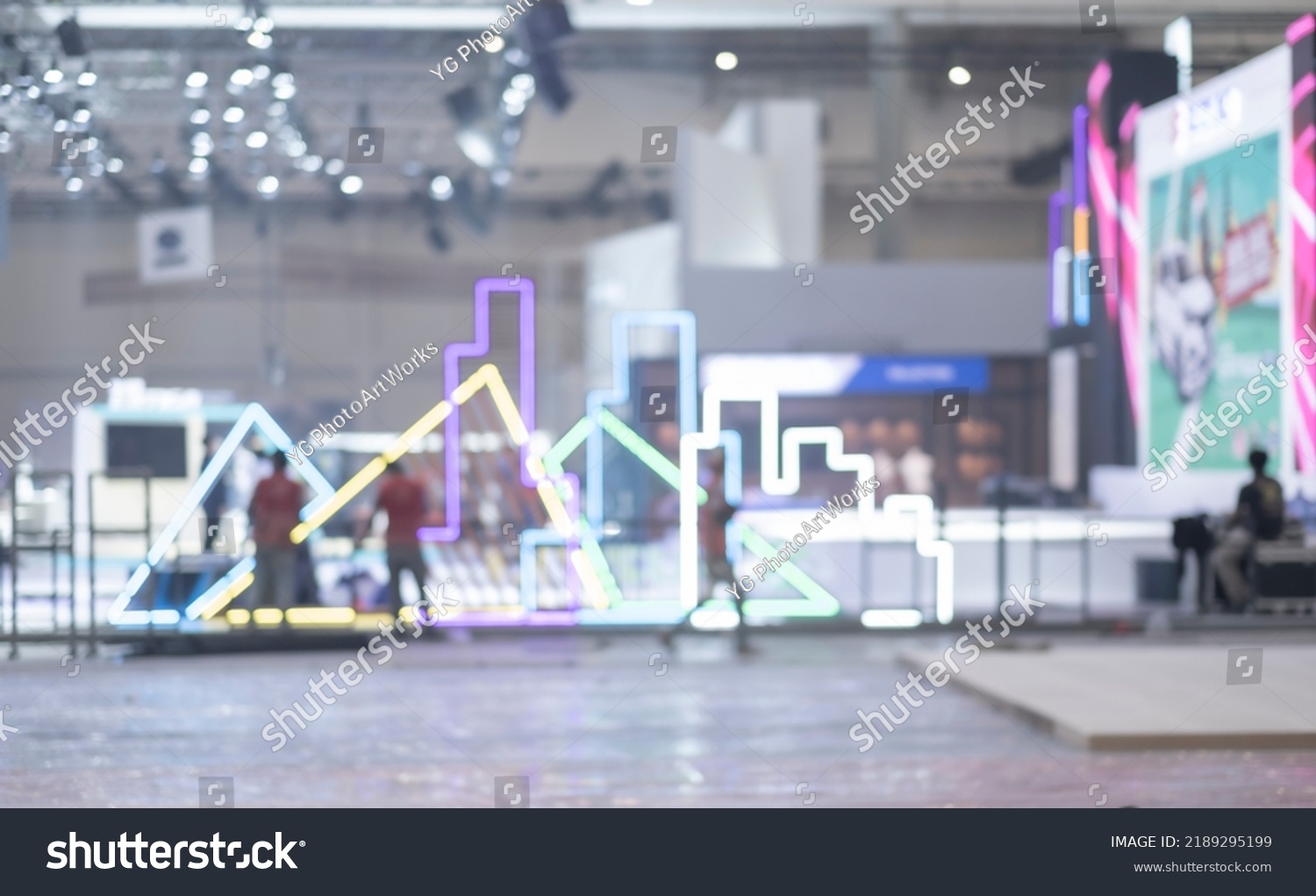 Blurry workers preparing exhibition event hall. Bokeh background of trade show business, world or international expo showcase, tech fair, with exhibitor trade show booth displaying product. #2189295199