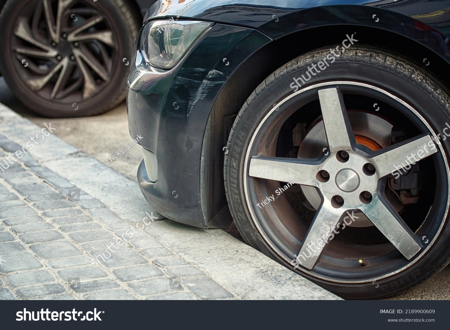 
Car wheel parked close to the curb on parking lot. 225.40r18 tire and bumper with scratch. Front side car parked close to the curb. Low clearance can cause bumper damage when parked close to the curb #2189900609