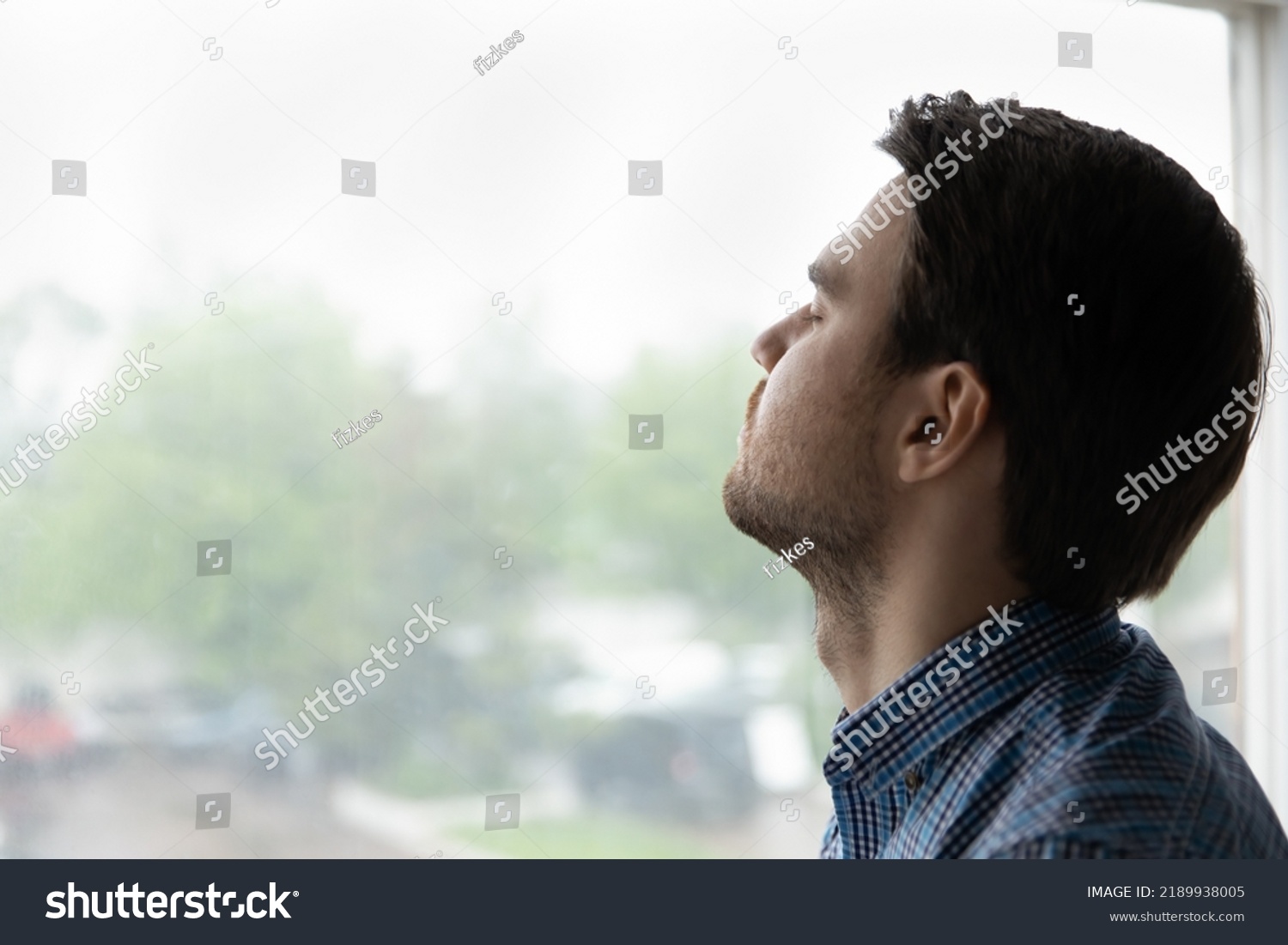 Close up of young 35s man closed his eyes pose on window background, guy take break, relieving fatigue or stress makes breath exercises, enjoy fresh conditioned air and climate control inside #2189938005