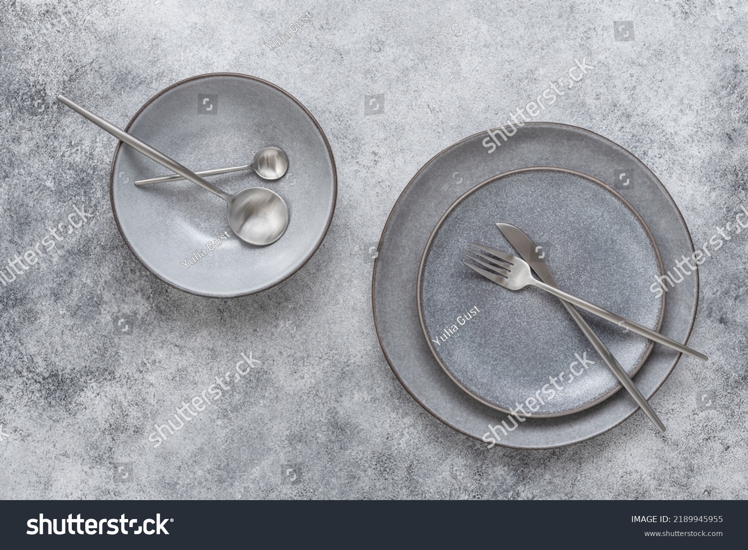 Gray ceramic plates and cutlery on a gray stone background. Modern craft crockery for table setting. Top view. #2189945955