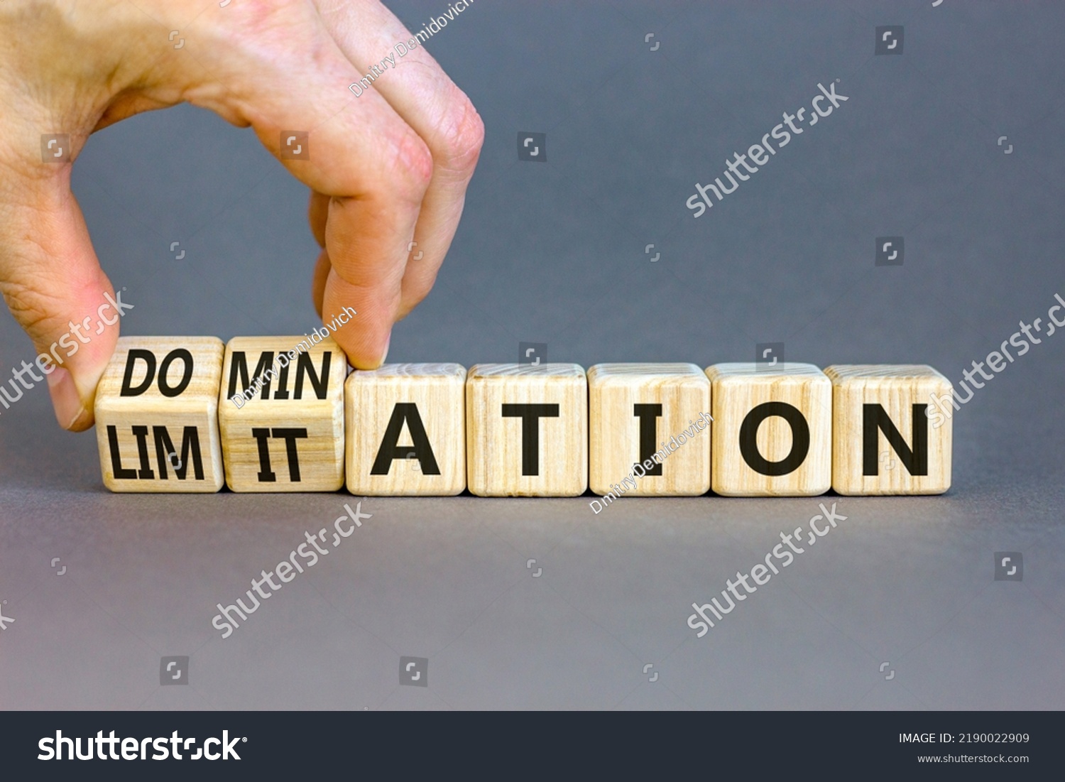 Domination or limitation symbol. Businessman turns cubes, changes the word domination to limitation. Beautiful grey table, grey background, copy space. Business, domination or limitation concept. #2190022909