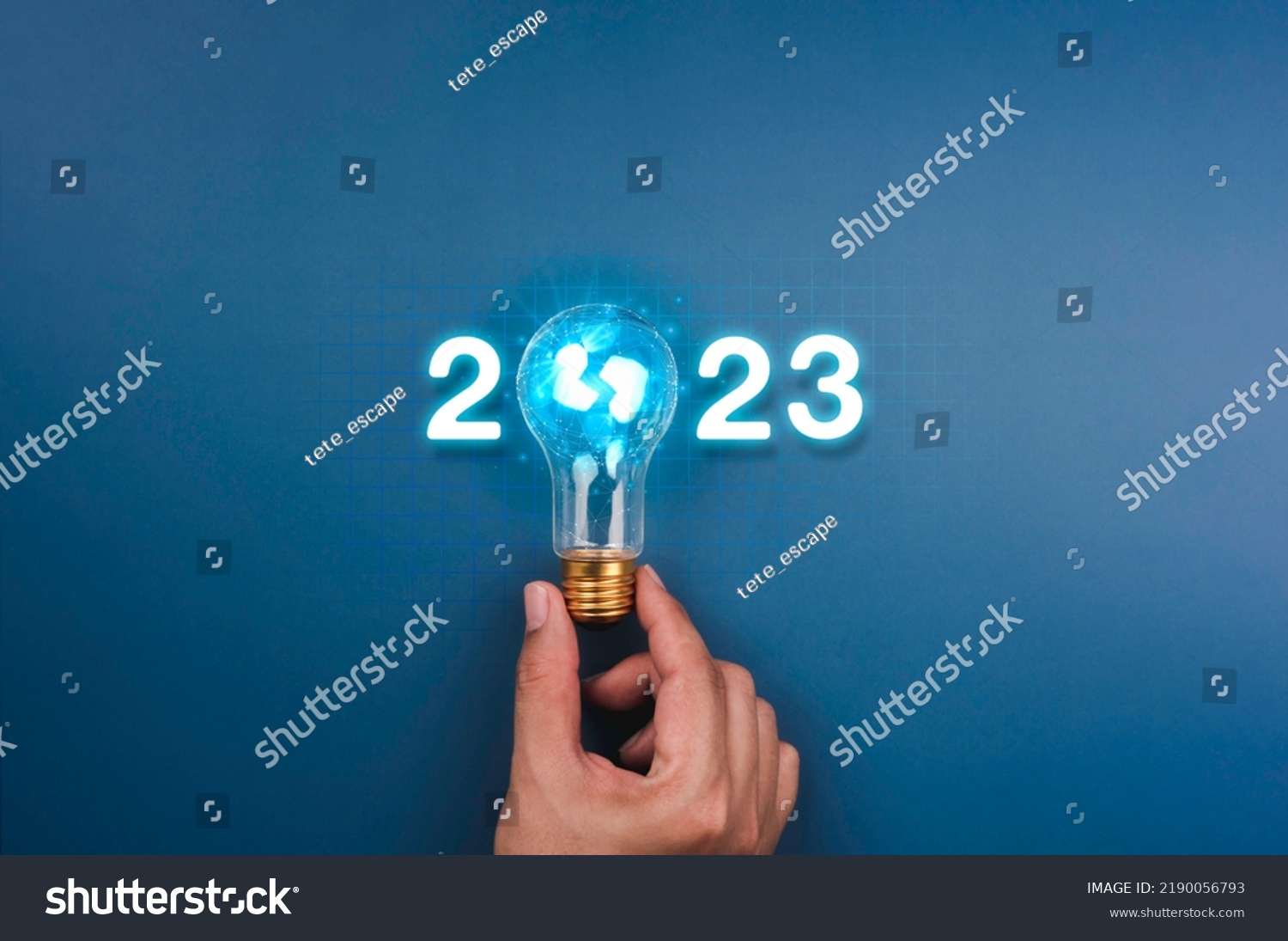 Shining 2023 calendar year numbers, neon style with creative trend light bulb holding by businessman's hand on digital network and blue background. Happy 2022 New Year greeting card with light bulb. #2190056793