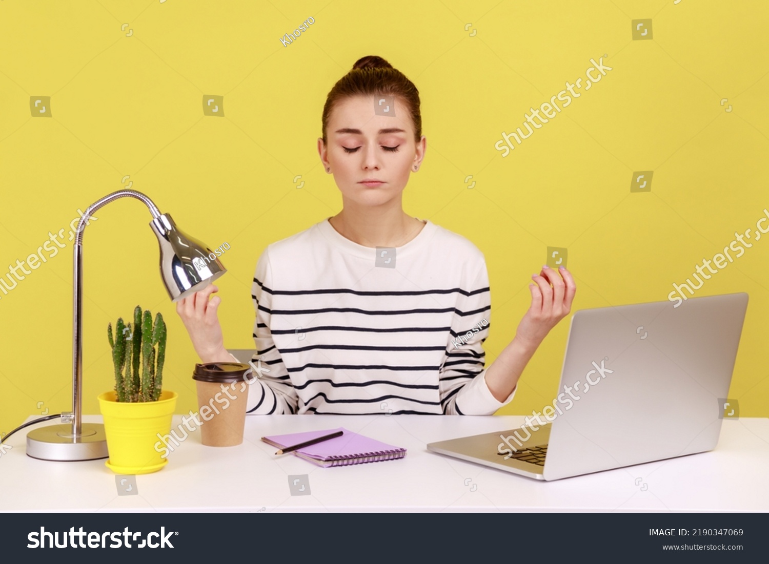 Peaceful mind, break at work. Calm woman sitting at workplace with laptop and raising hands in mudra gesture, meditating resting at home office. Indoor studio studio shot isolated on yellow background #2190347069