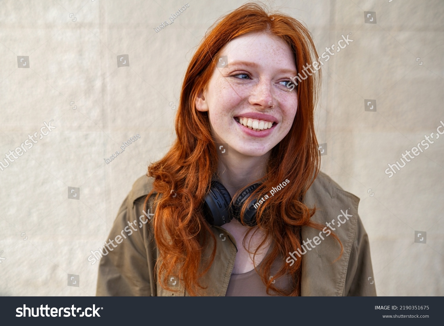 Happy teen stylish cool redhead fashion girl model standing on urban wall background laughing. Close up portrait of pretty joyful smiling teenage hipster girl with red hair looking away outdoors. #2190351675