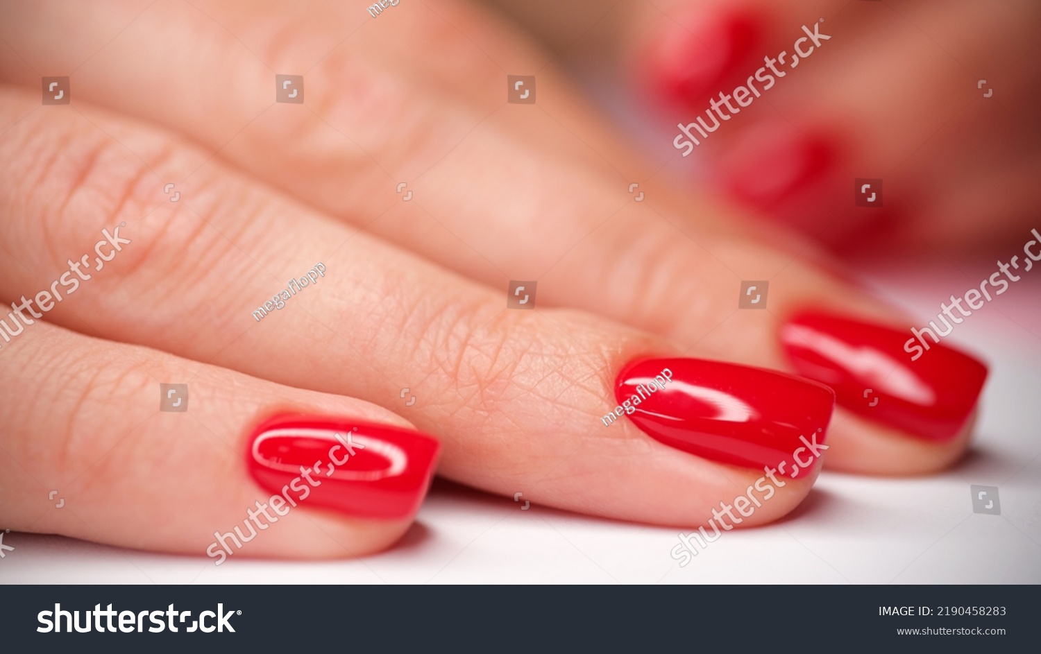Close-up of female hand with stylish bright red glossy manicure. Beautiful female fingernails with gel polish. Beauty salon and body care concept #2190458283