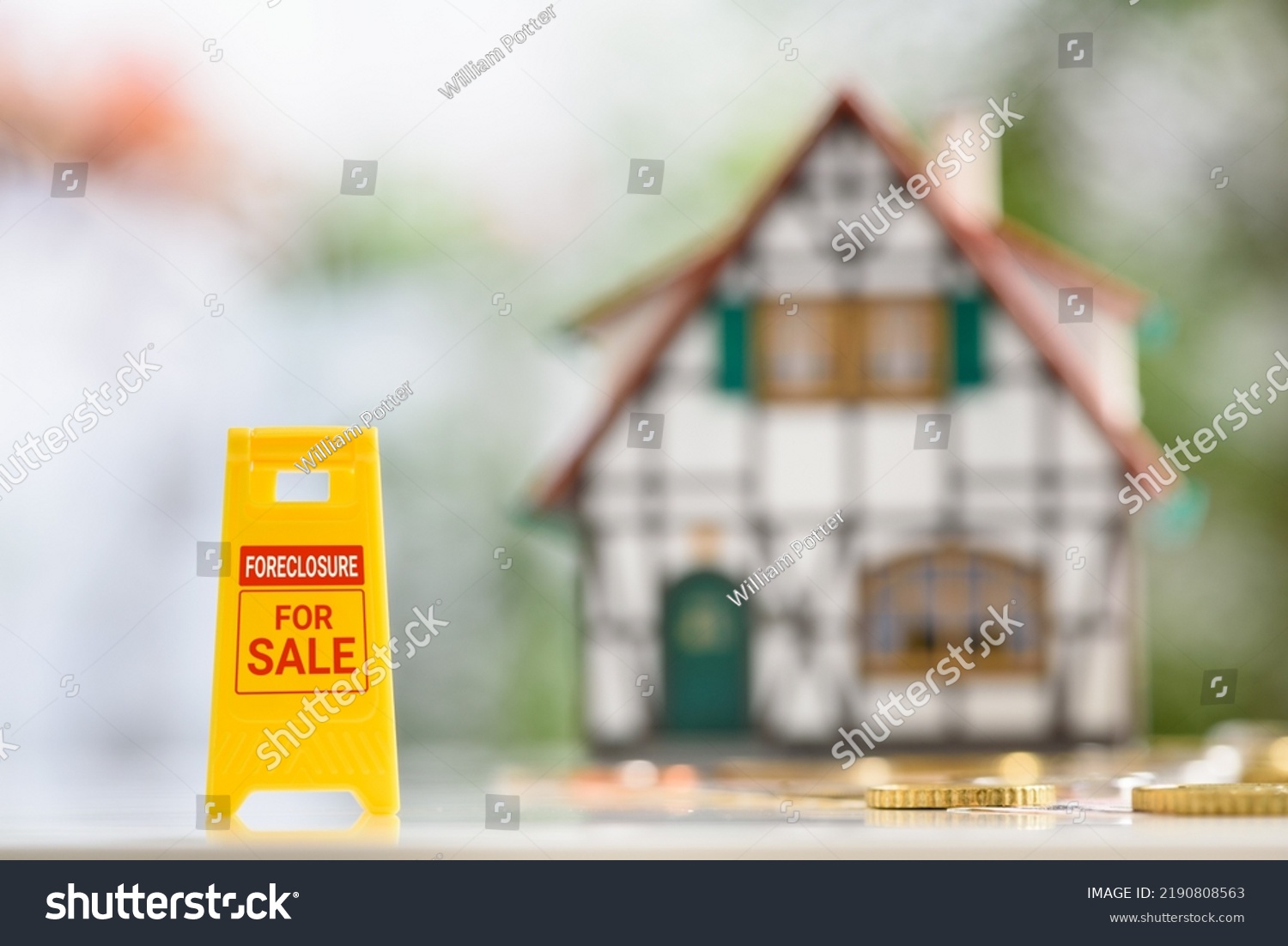 Foreclosures and foreclosed home for sale property listings, financial concept : Yellow warning sign board with the words FORECLOSURE FOR SALE, a two-story half-timbered model house, coins on a table. #2190808563
