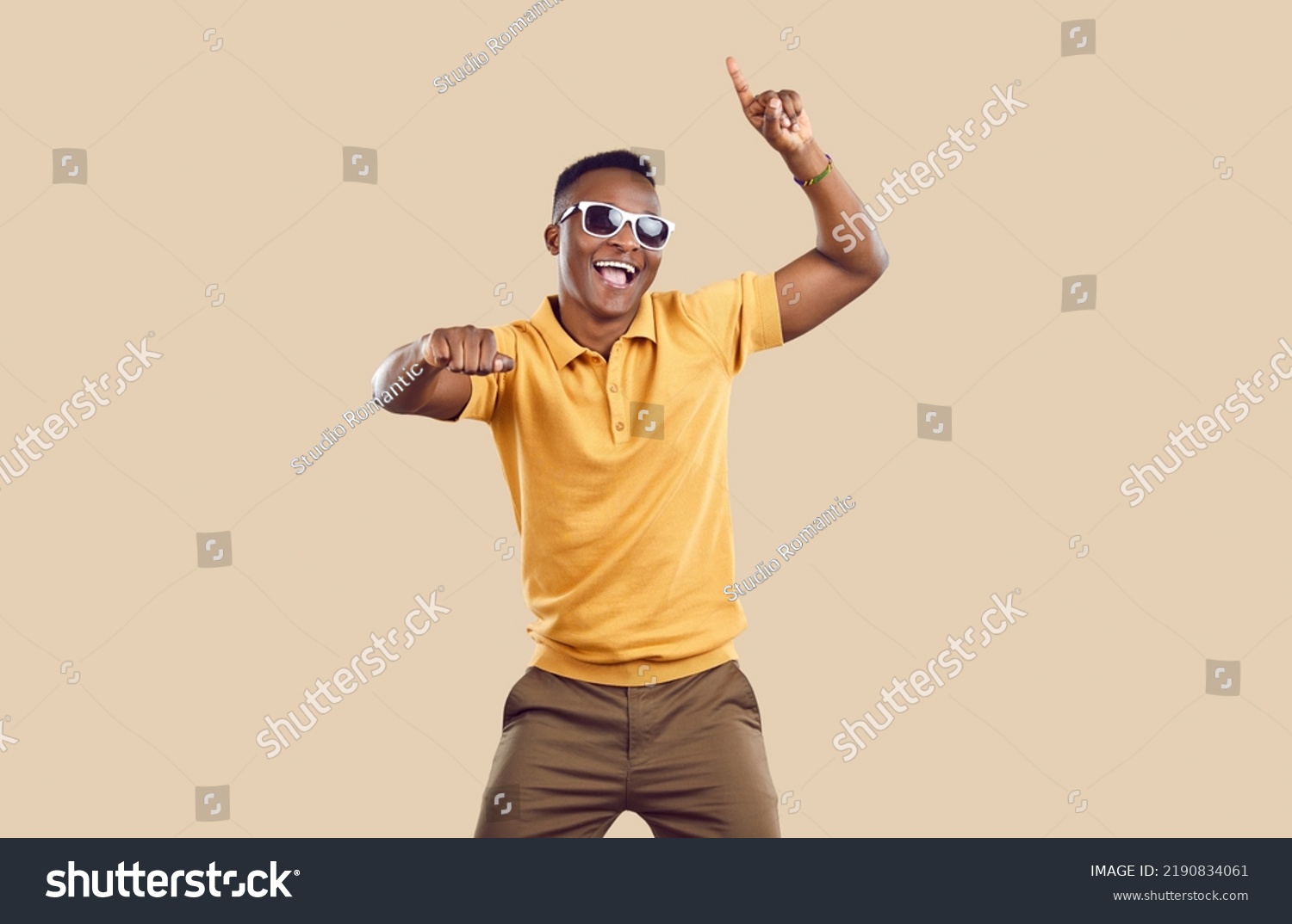 Portrait of happy handsome young African American man in casual clothes dancing in fashion studio. Cheerful attractive Tanzanian guy wearing yellow Tshirt and cool sun glasses dancing and having fun #2190834061
