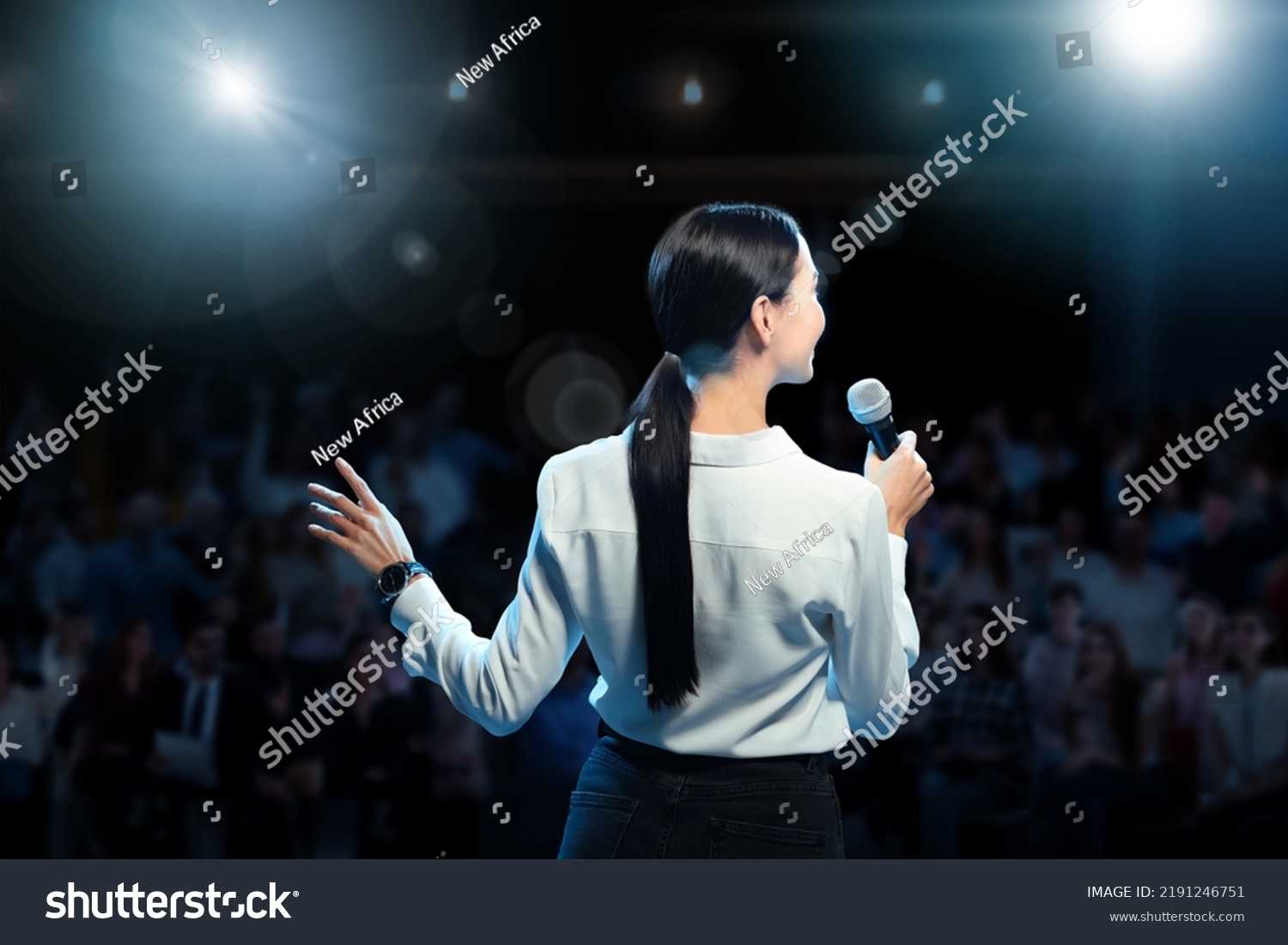 Motivational speaker with microphone performing on stage, back view #2191246751