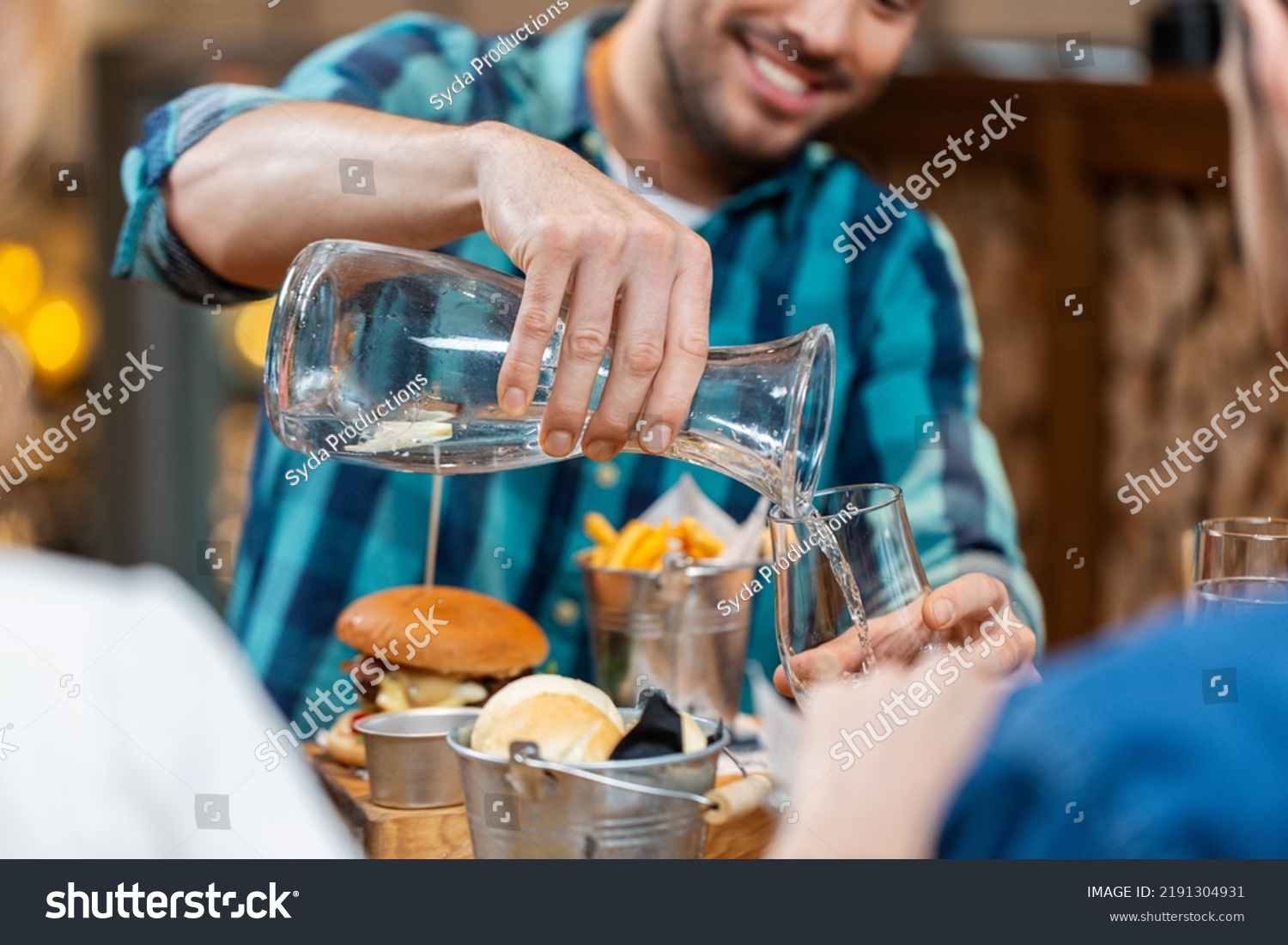 food, leisure and people concept - happy smiling man having dinner at restaurant and pouring water from jug to glass #2191304931