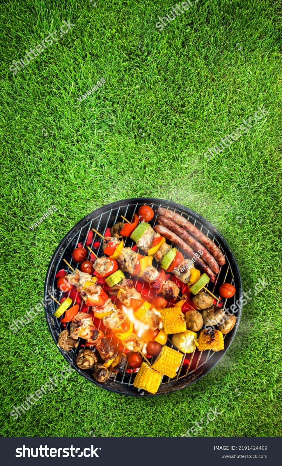 Top view of bbq grill, grilled meat, vegetables, mushrooms with flames and smoke. Placed on green grass lawn. Grilled food, vertical composition. #2191424409