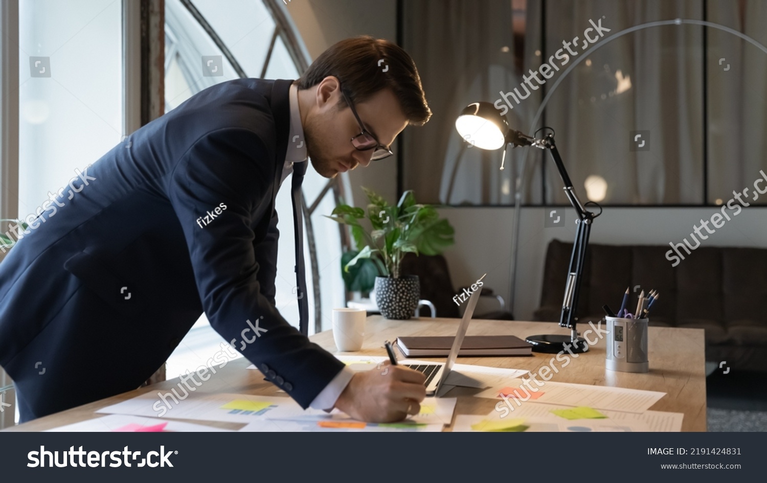 Close up confident businessman wearing glasses writing notes on colorful stickers, entrepreneur executive working with documents, analyzing financial project statistics, standing at table in office #2191424831