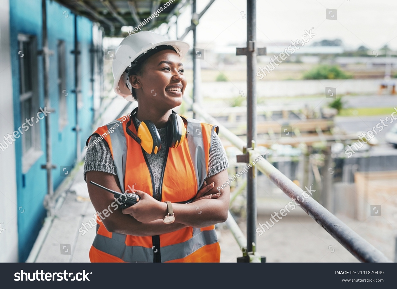A happy, smiling and cheerful young black woman or senior construction industry worker standing at a building site. A professional female employee working at housing or property development location #2191879449