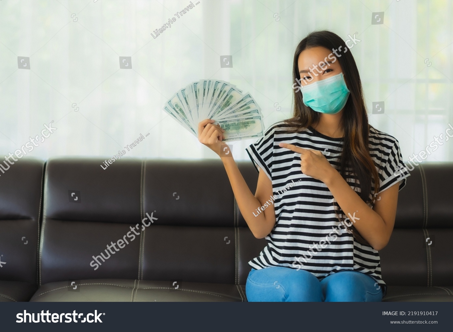 Portrait beautiful young asian woman with mask on sofa show money or cash at home #2191910417