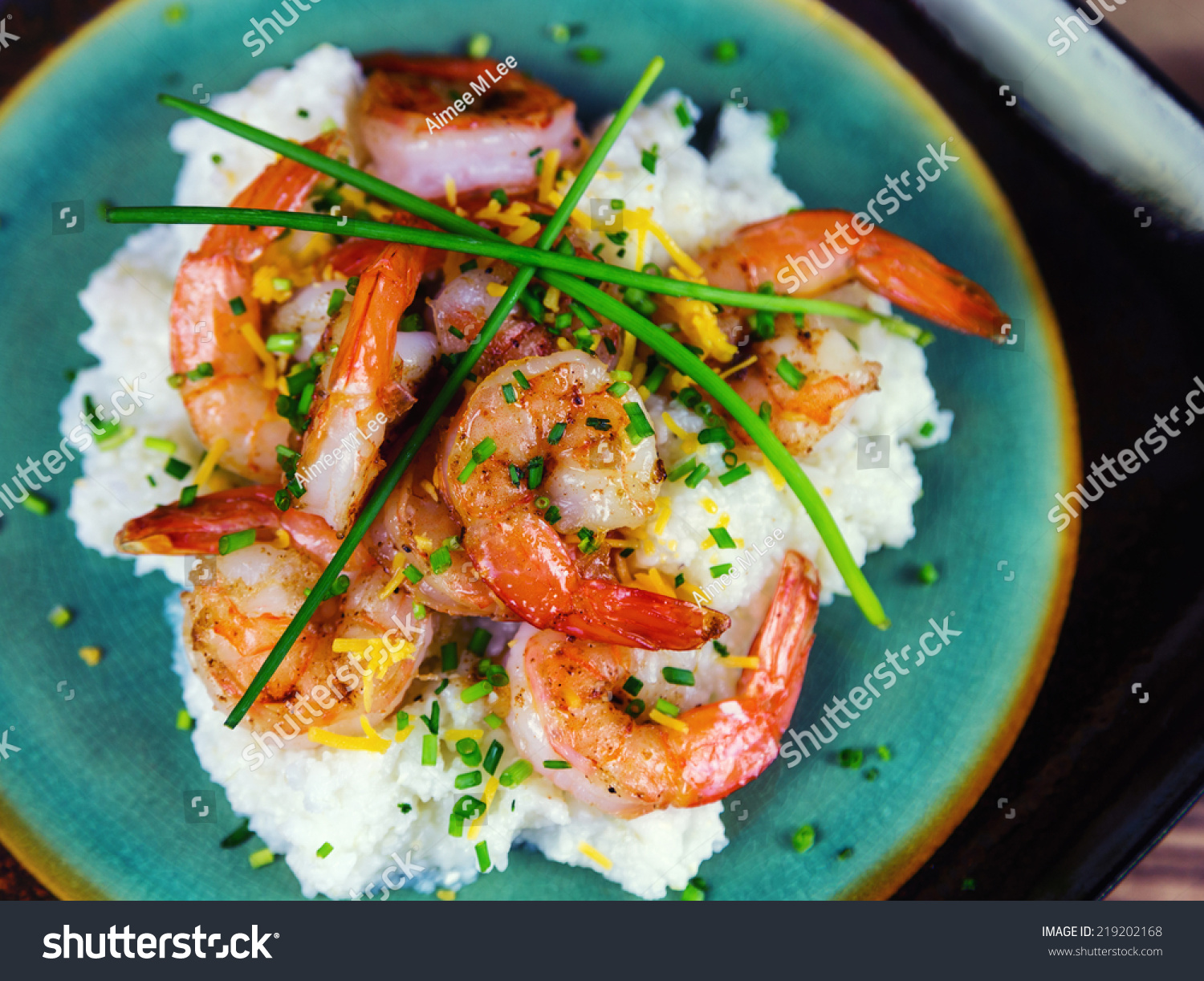 Shrimp and grits with cheese and chives on a rustic plate.  #219202168