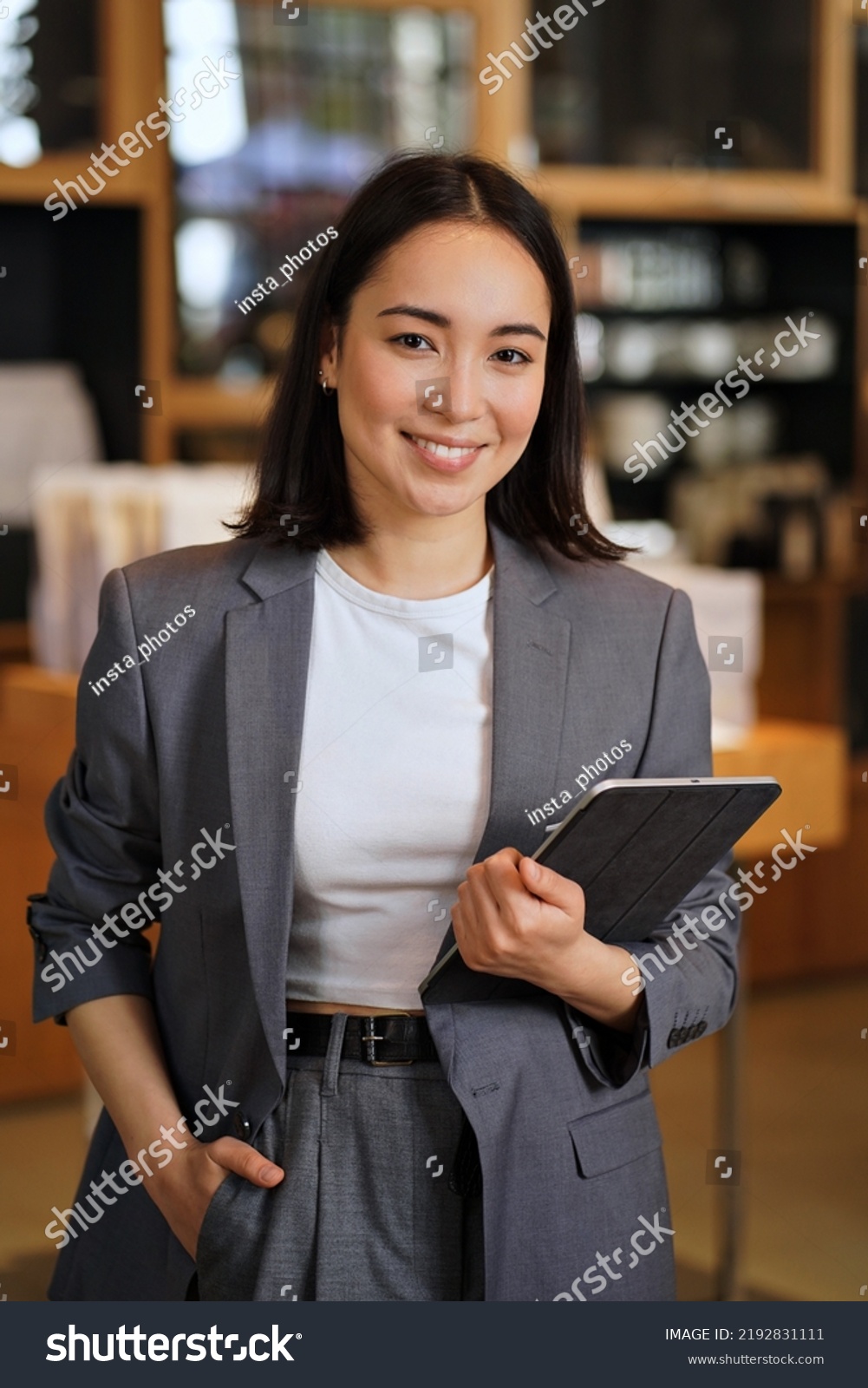 Young smiling successful professional leader Asian business woman, female executive manager, saleswoman wearing suit holding digital tablet standing in office looking at camera, vertical portrait. #2192831111
