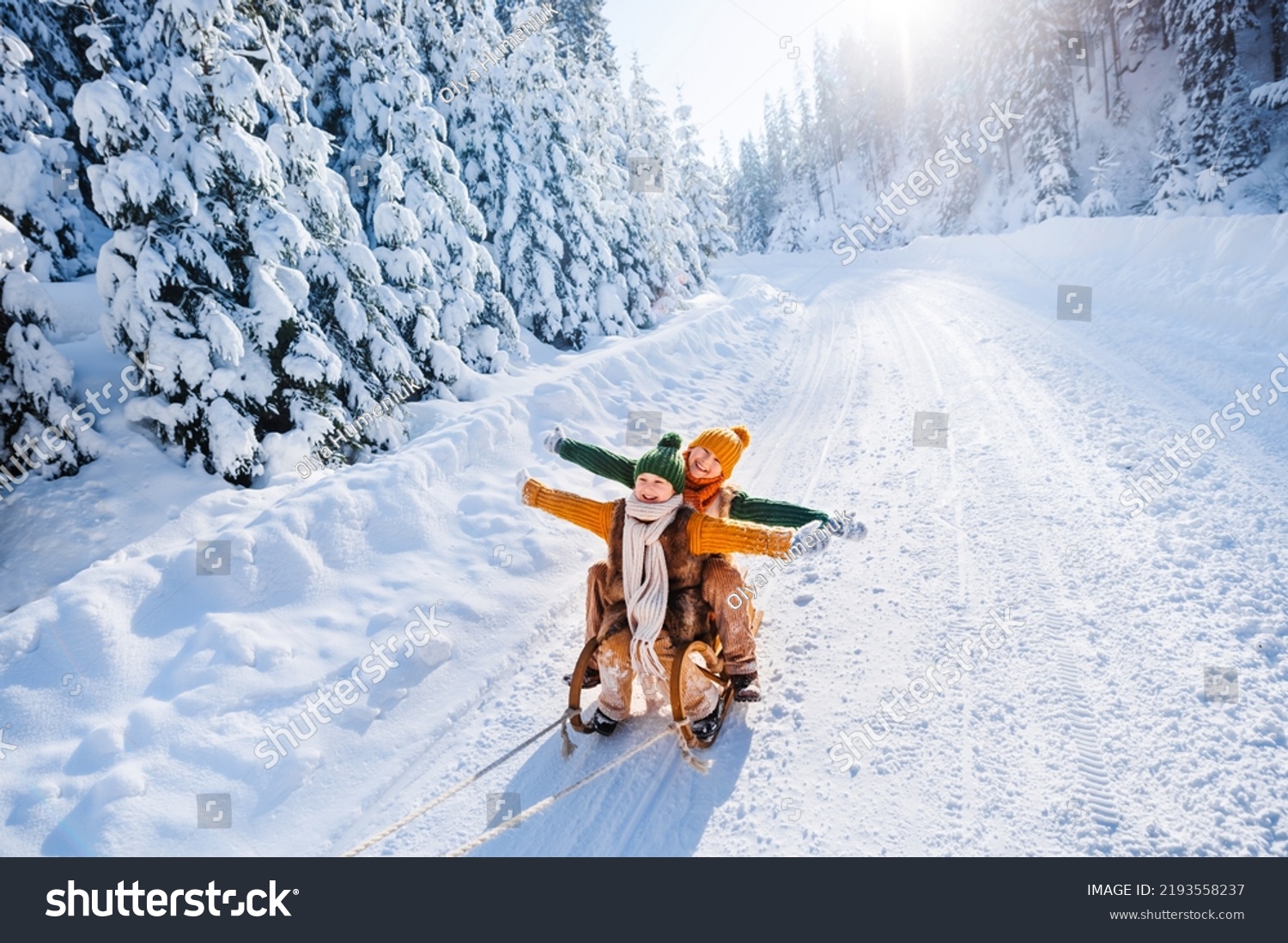 Happy funny children ride wooden retro sleds on snowy road in mountains. Family on winter walk. #2193558237