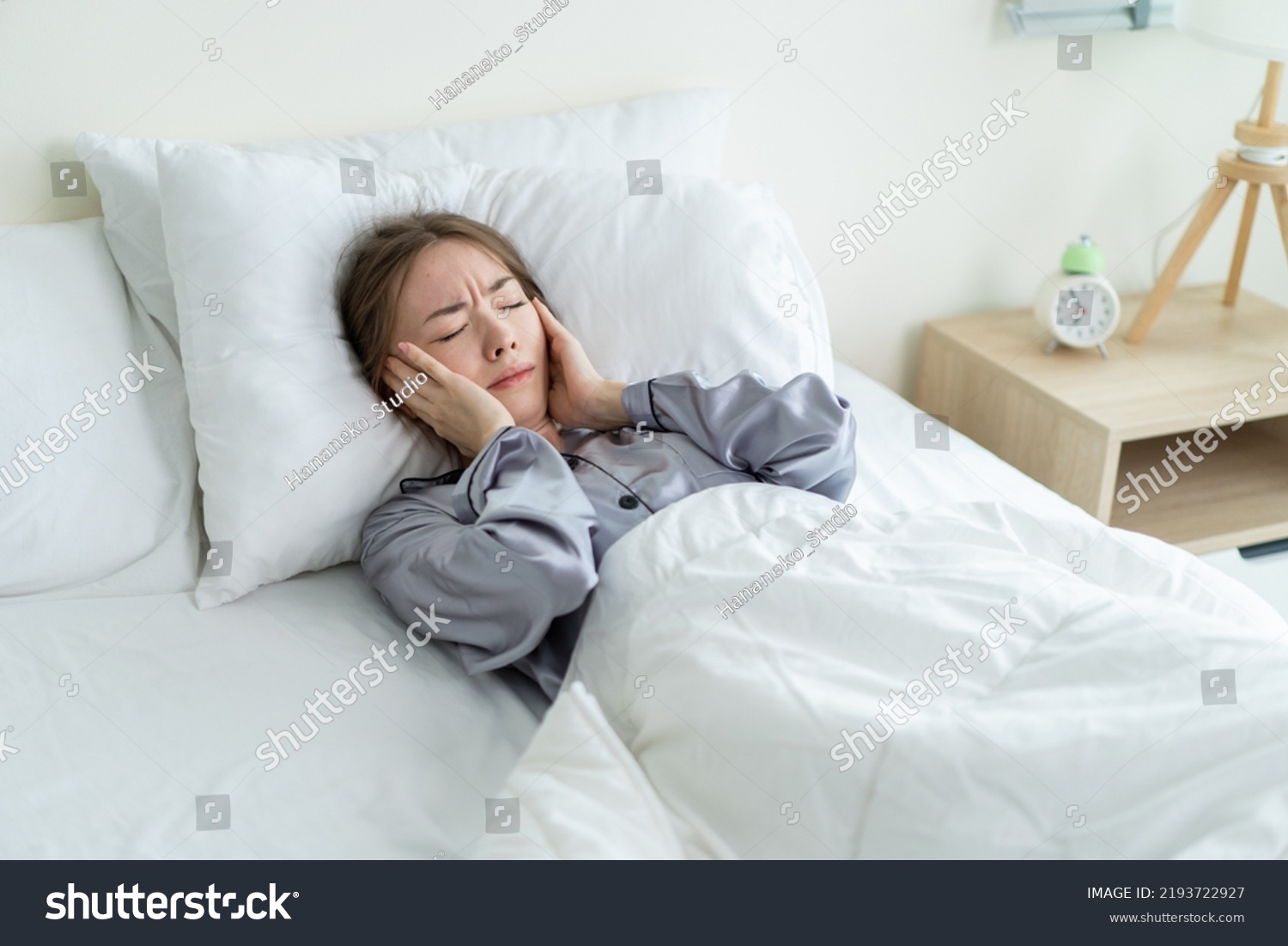 Caucasian beautiful frustrated girl in pajamas sleep on bed in morning. Attractive young woman lying down with upset and angry feeling due to noise and put cozy blanket on her ears in bedroom in house #2193722927