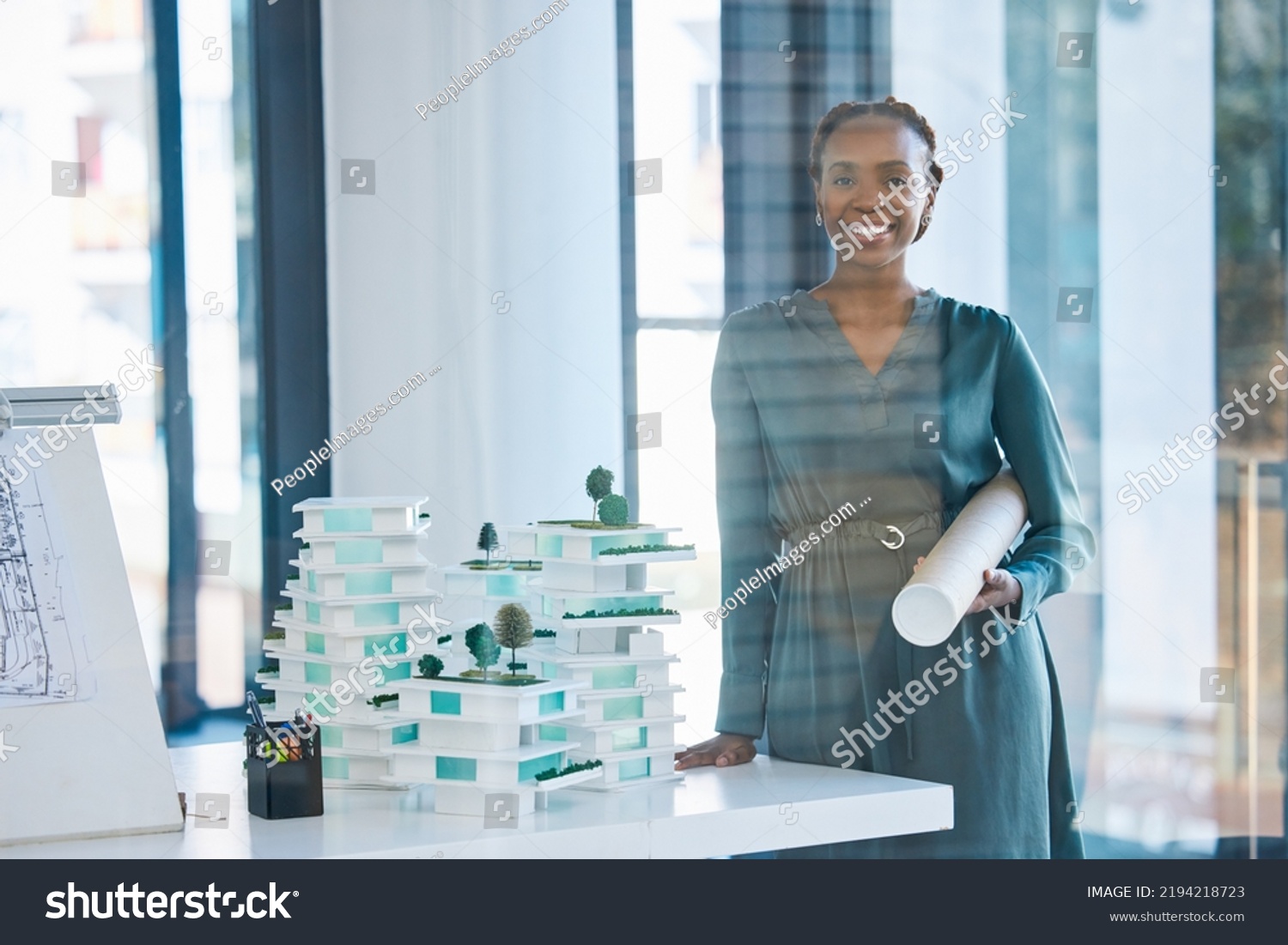 Architect, engineer and designer holding a blueprint with a positive mindset, mission and vision in an office. Portrait of a black woman standing next to 3D representation of proposed building #2194218723