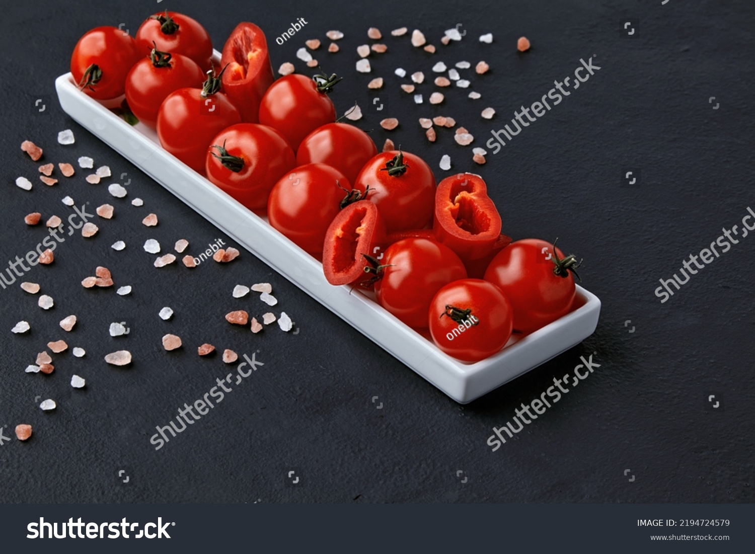 An elongated plate of tomatoes, paprika and coarse pink Tibetan salt on a black concrete table. High angle with copy space #2194724579