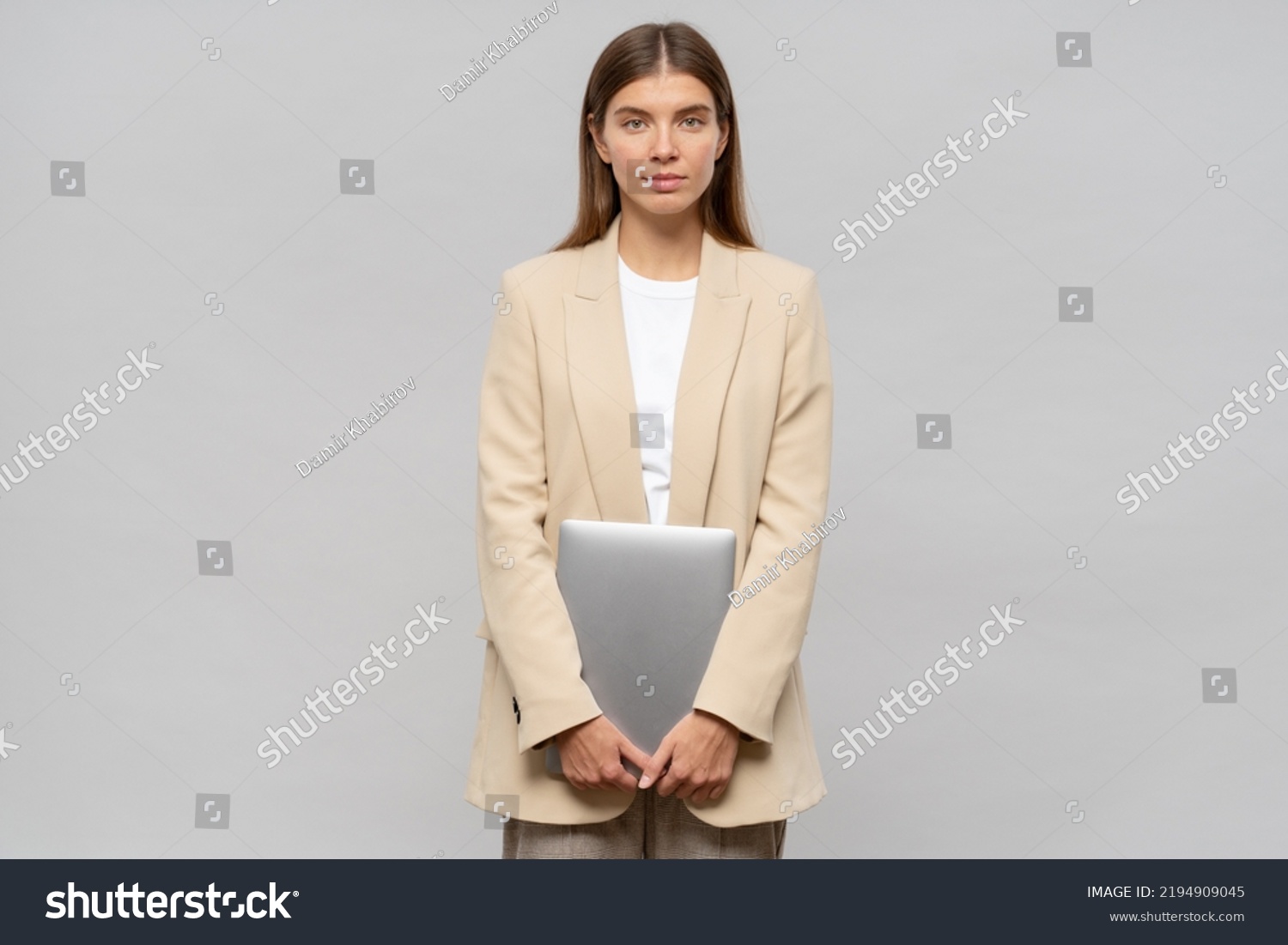 Shy female student feeling nervous waiting for results of exam standing on gray background with laptop in hands. Education and technology #2194909045