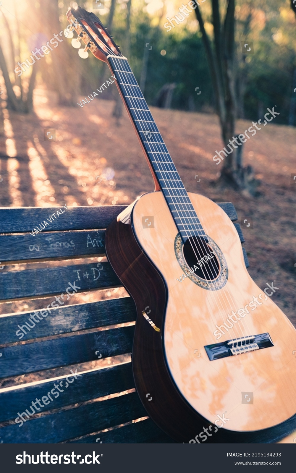 Beautiful classical guitar on a bench in the park with lens flare. Photo of a new wooden guitar with nylon strings outdoors in the summer during sunset. No people. Beautiful string instrument. #2195134293