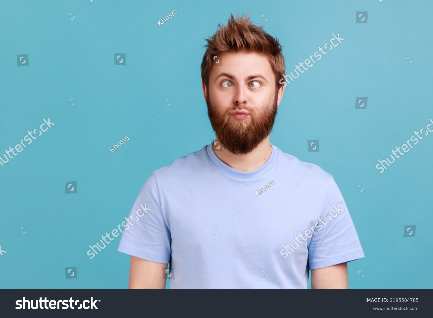 Portrait of man making silly humorous face with eyes crossed, showing comical silly brainless facial expression posing with stupid smile, fooling around. Indoor studio shot isolated on blue background #2195584785